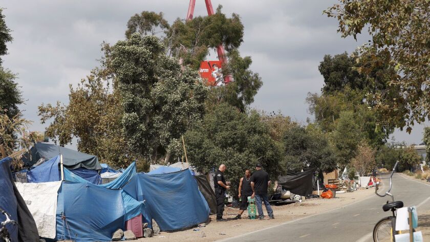 An Anaheim police officer speaks to a resident of the large homeless encampment along the Santa Ana River Trail next to Angel Stadium.