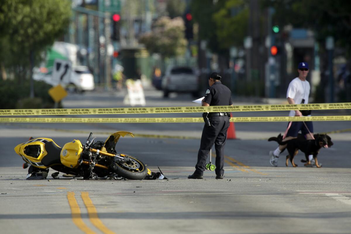 A man walks by with his dogs as an LAPD officer investigates a fatal hit-and-run incident in North Hollywood in July.