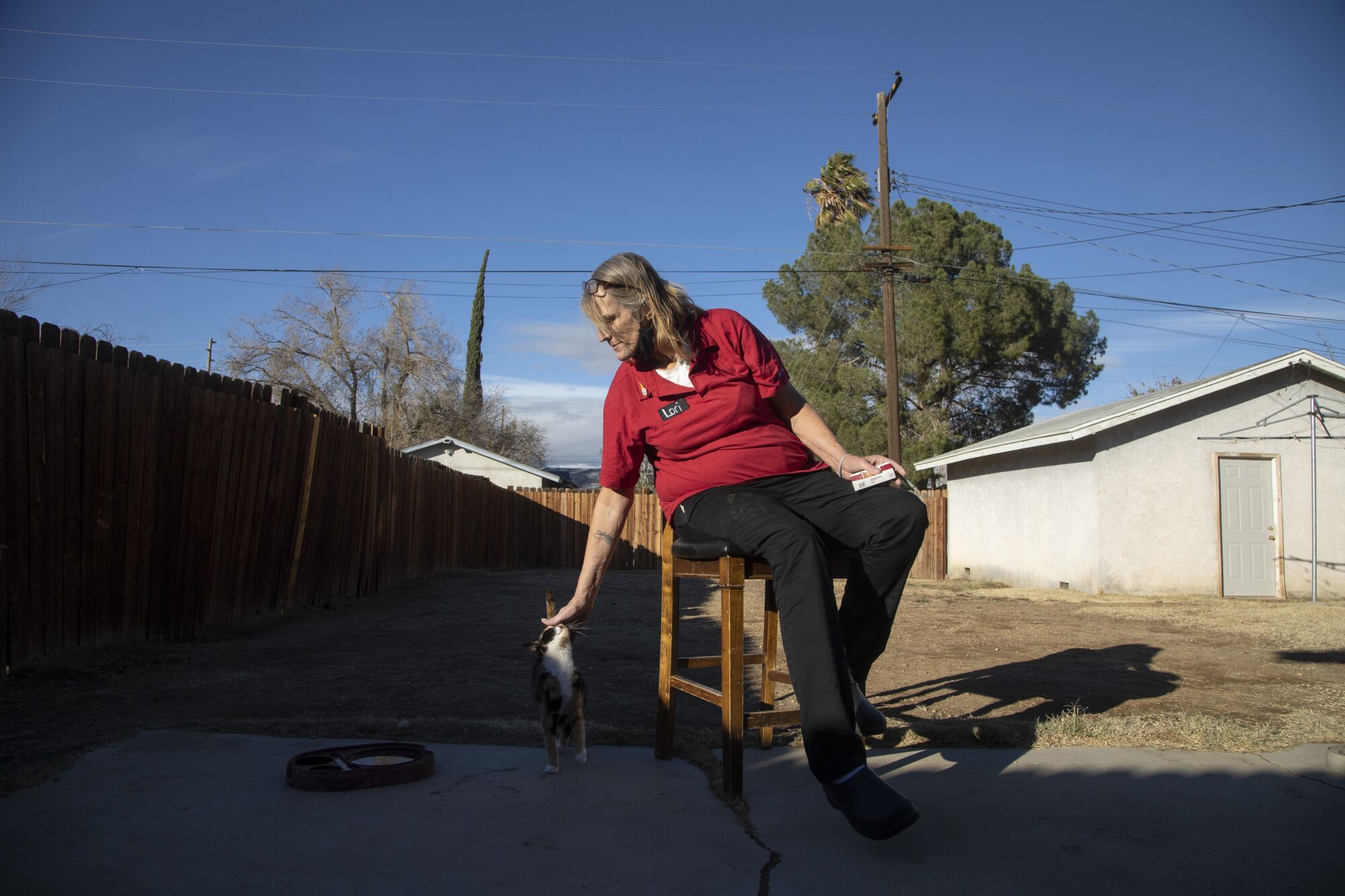 Lori Castro pets a stray cat while smoking a cigarette in the backyard of a shared house in Palmdale.