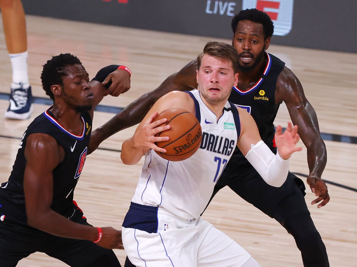 Dallas Mavericks' Luka Doncic is pressured by Clippers' Reggie Jackson and JaMychal Green.