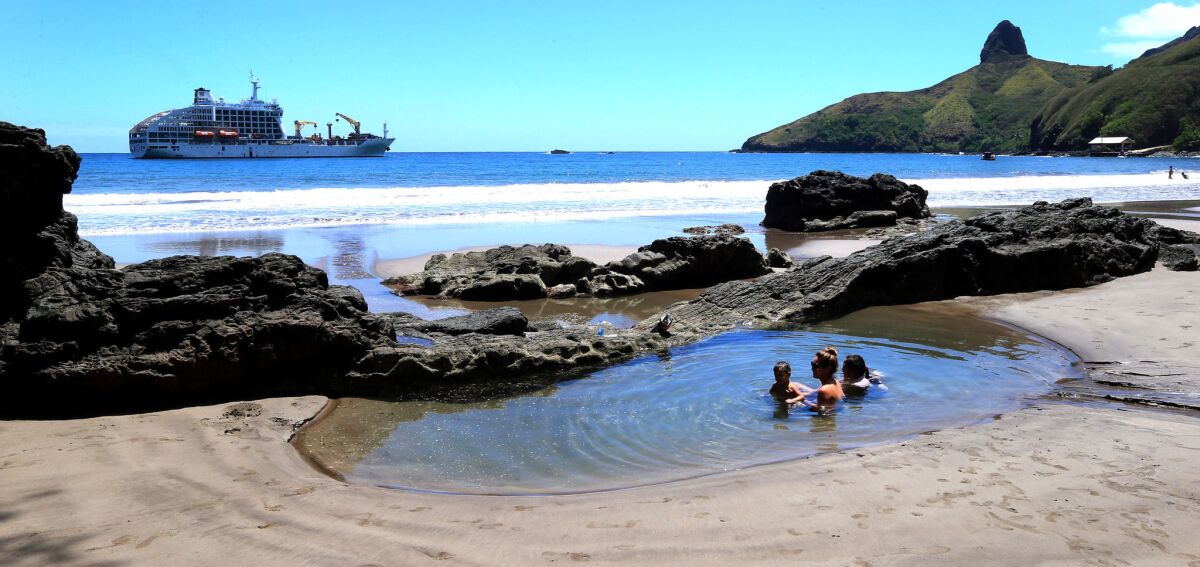 A local Hiva Oa Island family plays in a natural ocean pool as the Aranui 5 ship anchors, background. Hiva Oa is part of the Marquesas chain of Islands.
