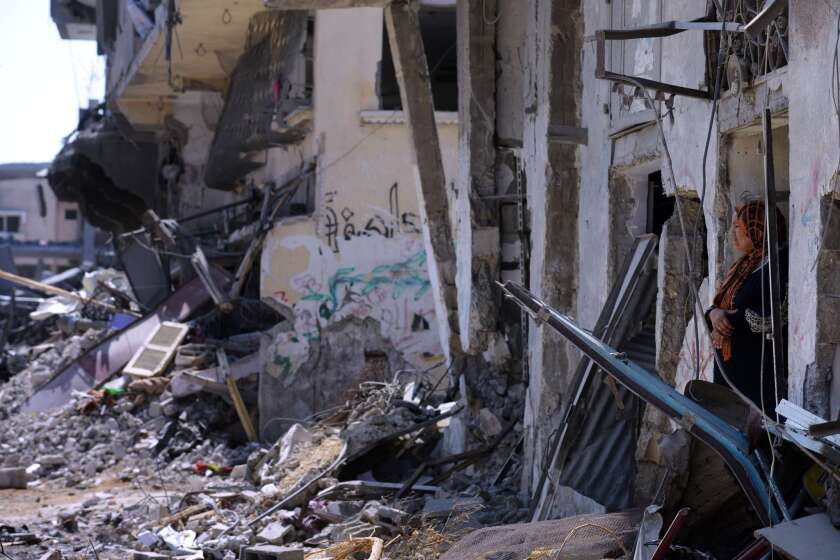 A Palestinian woman stands in the front door of her damaged home in Gaza.