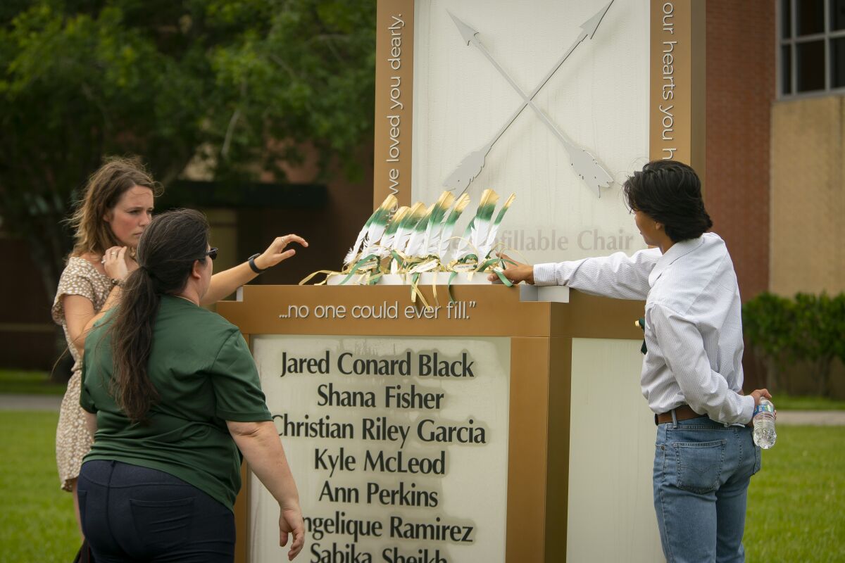 Corrigan Garcia, who graduated from Santa Fe High School in 2018, and Maegan Huddleston, who graduated in 2019, and Megan Grove, who chair's the Santa Fe Ten Memorial Foundation, place ten feathers representing the ten victims of the 2018 Santa Fe school shooting on the new memorial to the ten victims, Tuesday, May 18, 2021, outside of the high school in Santa Fe, Texas. The Santa Fe Ten Memorial Foundation unveiled the "Unfillable Chair," a student designed memorial, on the third anniversary of the shooting. The foundation is planning a larger memorial for the future. (Mark Mulligan/Houston Chronicle via AP)