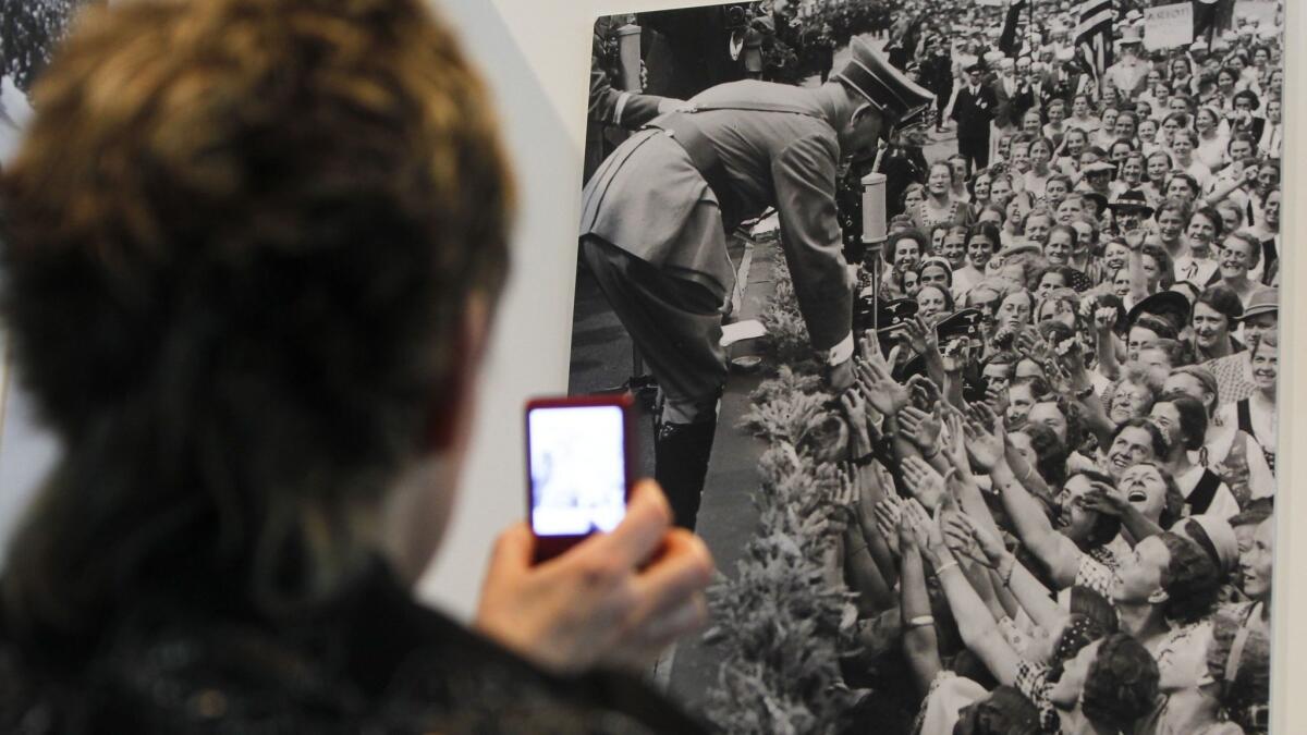 A woman takes a picture of a photograph showing Adolf Hitler with a crowd of supporters in Berlin.