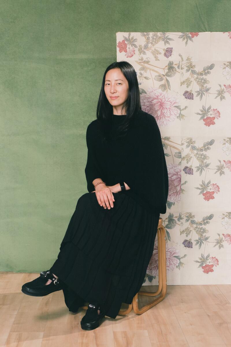 Christina sits on a stool in front of a green and floral backdrop