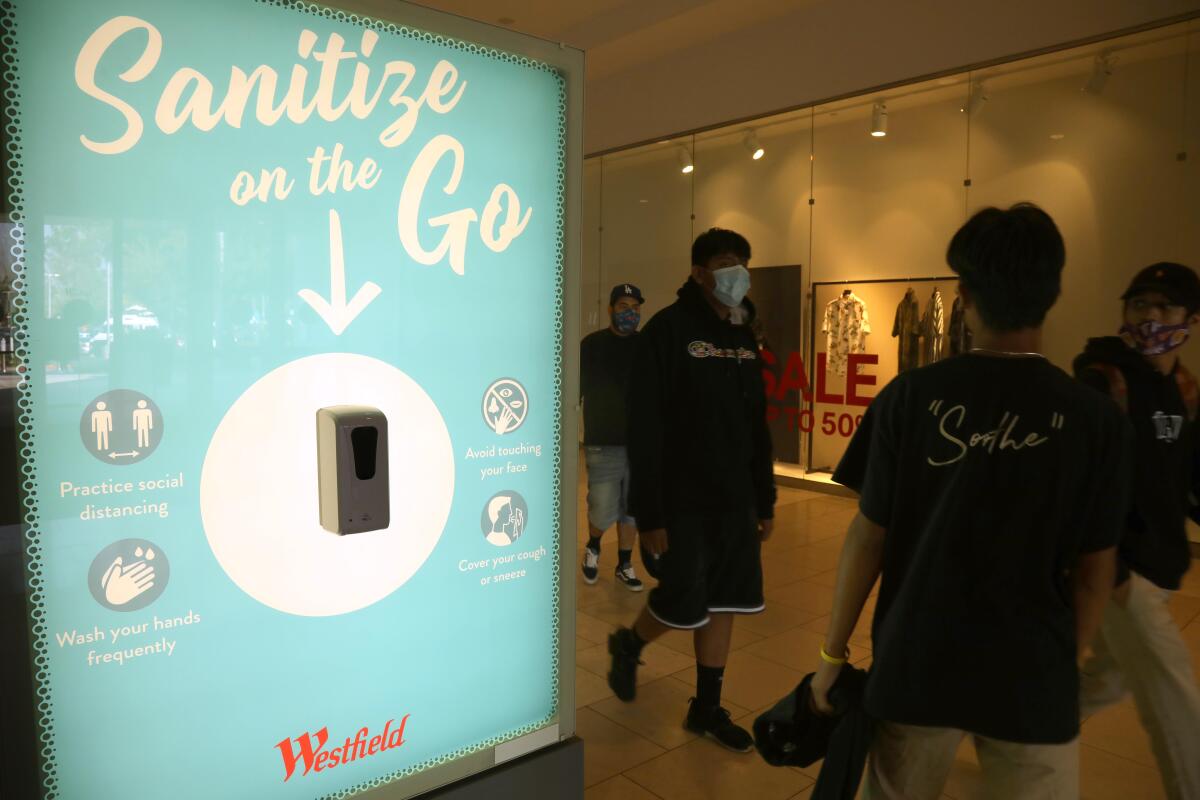 Shoppers walk past a hand sanitizer station at Westfield Santa Anita.