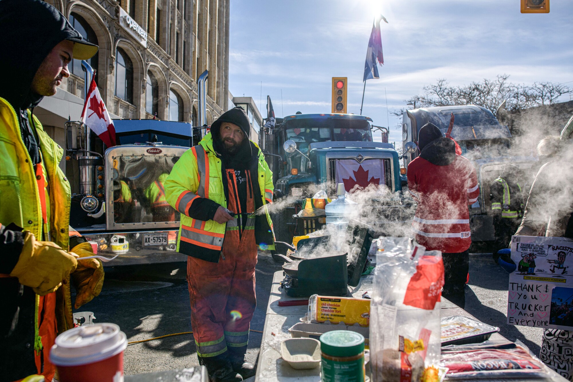 Steam rises from pans as demonstrators cook breakfast on the side of the street with big-rigs in the background