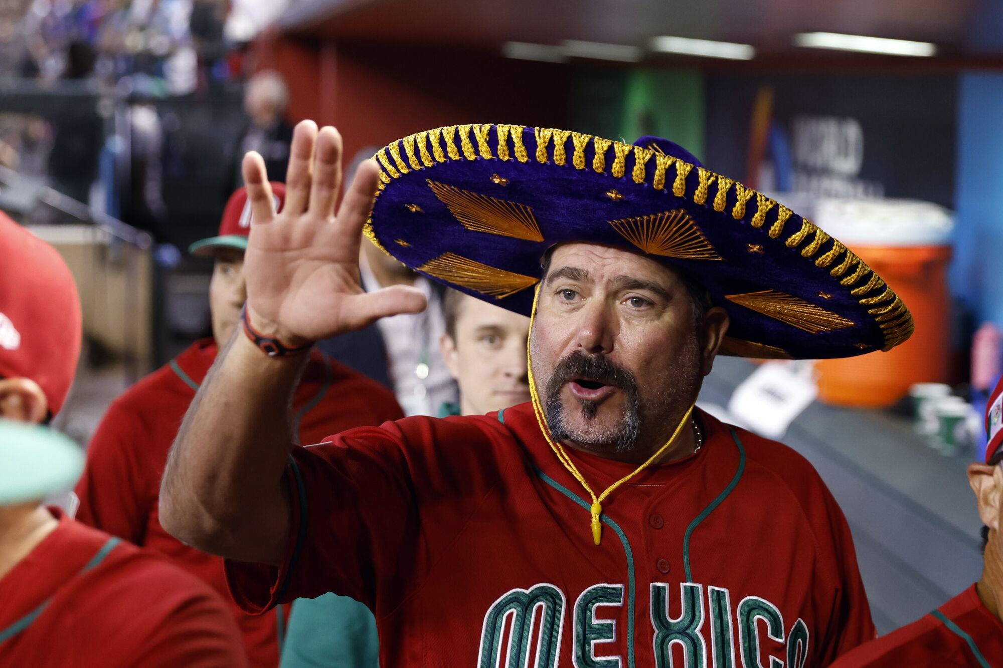 Mexico manager Benji Gil celebrates waves his hand while wearing a purple sombrero in the dugout.