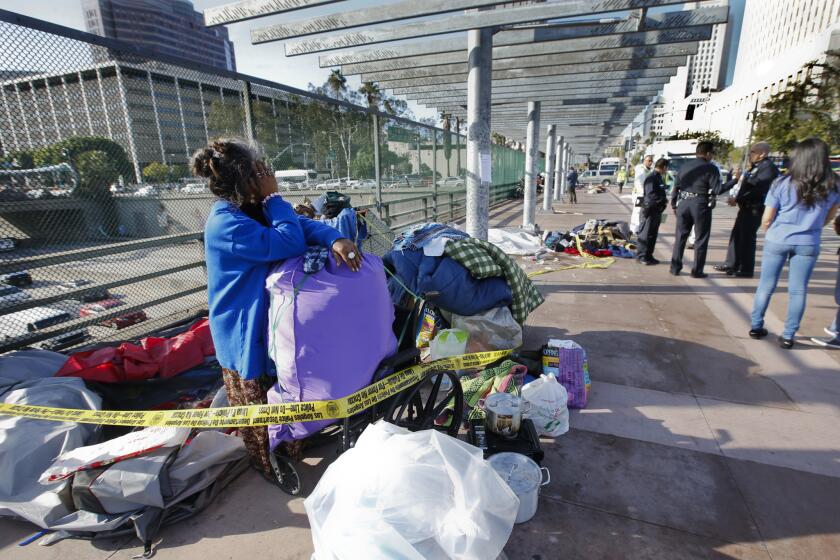 Ry Thounry packs up her tent on the Main Street overpass above the 101 Freeway in downtown Los Angeles while sanitation crews move in to clean the homeless encampment.