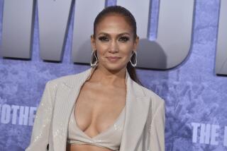 Jennifer Lopez posing in a sparkly suit, bra and earrings against a purple background.