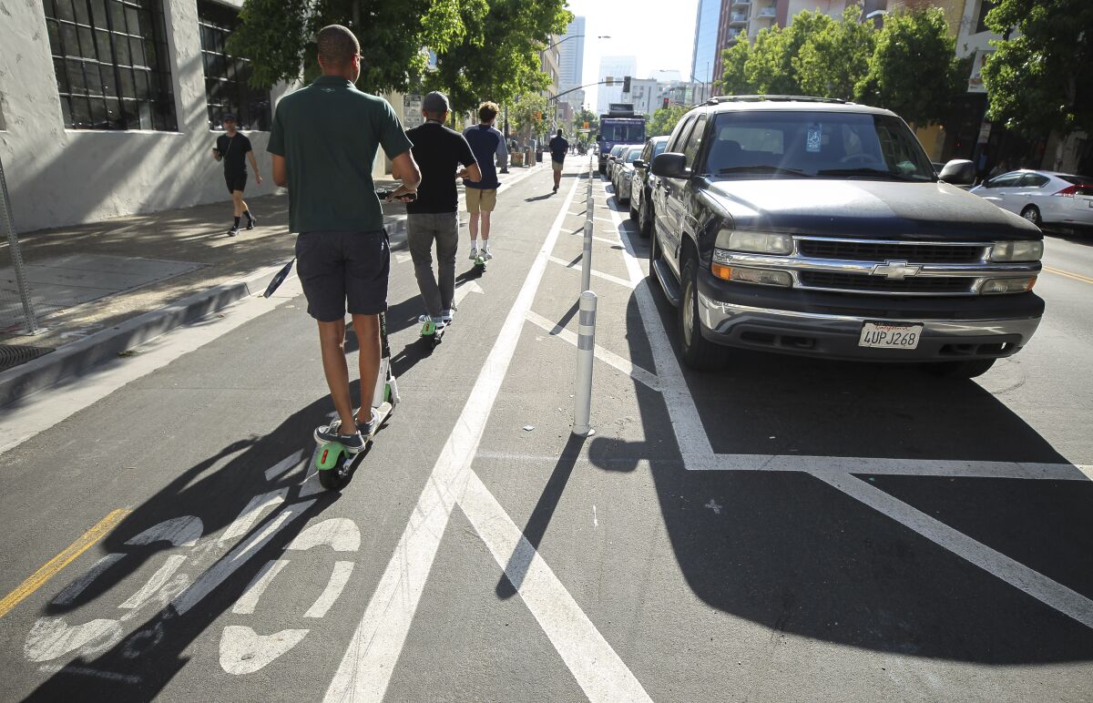 People riding electric scooters use a bike lane next to where cars park away from the curb on J Street, near the 11th Avenue intersection in downtown San Diego on Tuesday.