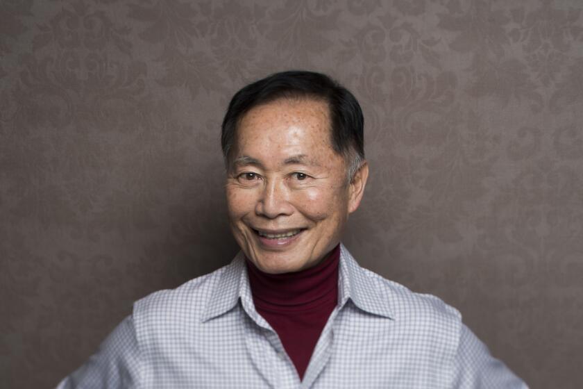 A man in a dress shirt smiles and poses with his hands on his hips