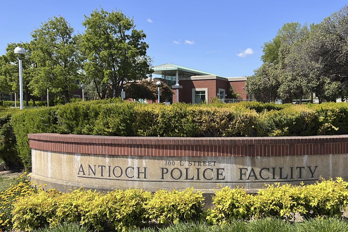 A short wall reading "Antioch Police Facility" in front of shrubs and trees outside a brick building