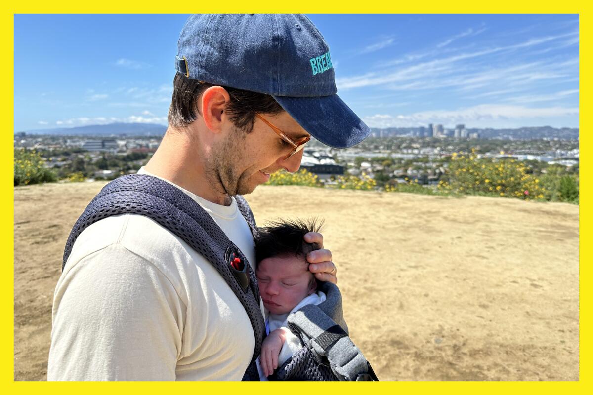A man in a baseball cap and sunglasses carries his newborn in a BabyBj?rn while hiking