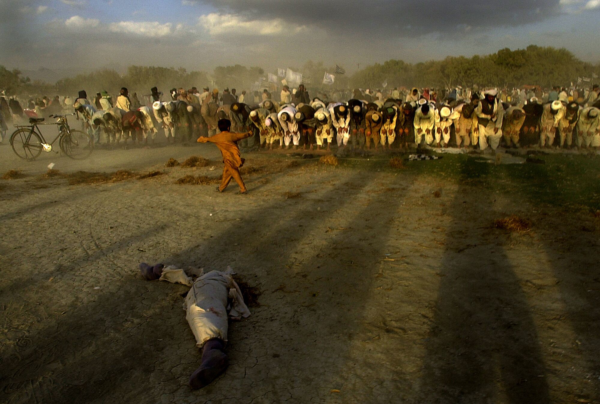 A boy pirouettes in the wind between a dismembered doll and Muslim men kneeling in prayer on Nov. 2, 2001.