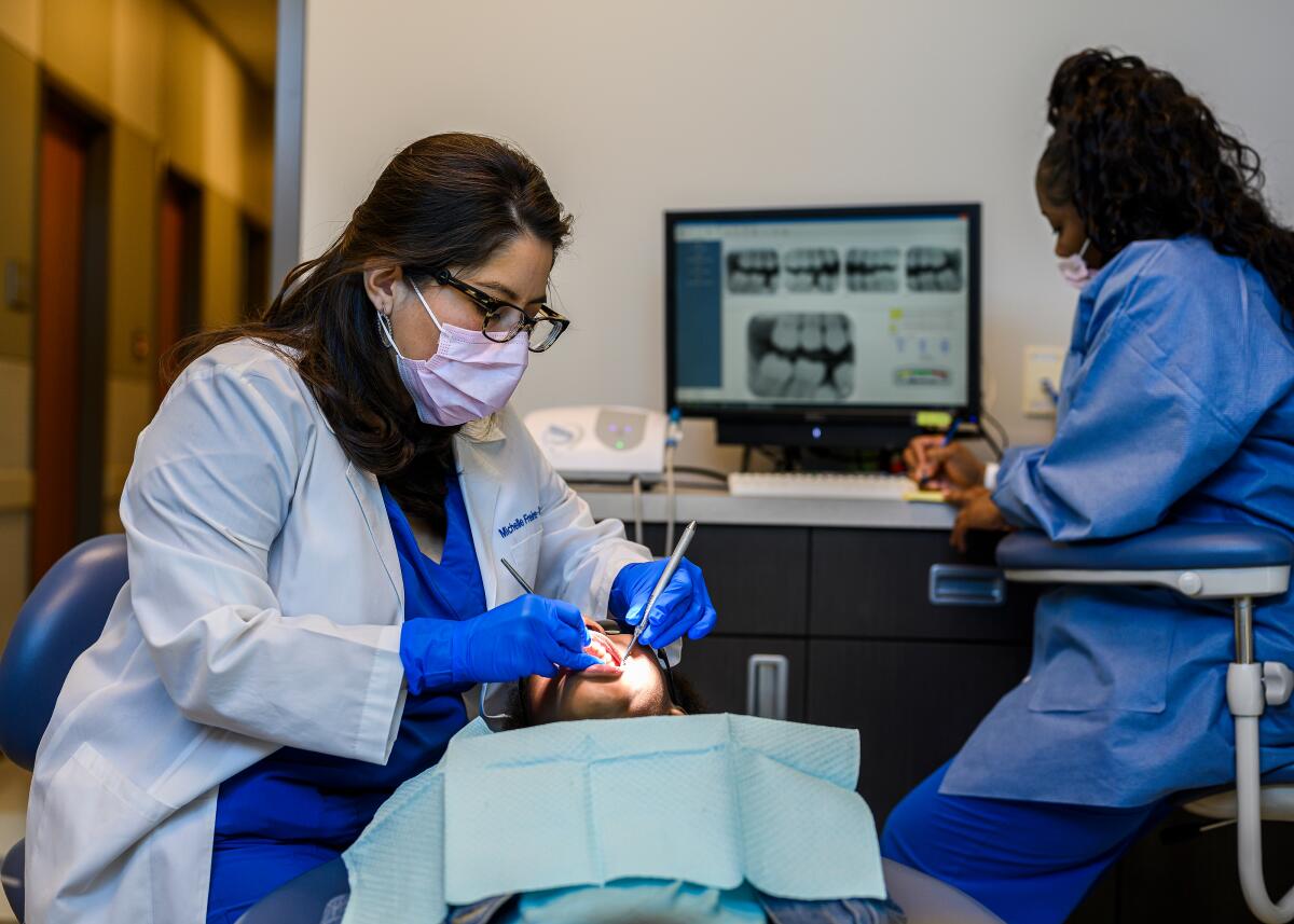 Dentist Michelle Freire-Troxel, from left, cleans the teeth of Amari Harris.