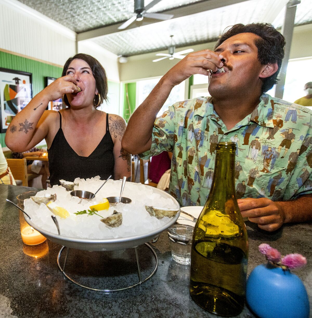 A woman and a man slurp oysters at a restaurant.
