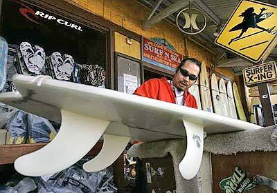 Richard Samiley scrapes the wax off a surfboard being prepared for consignment at the Surf 'N Sea shop in Haleiwa.