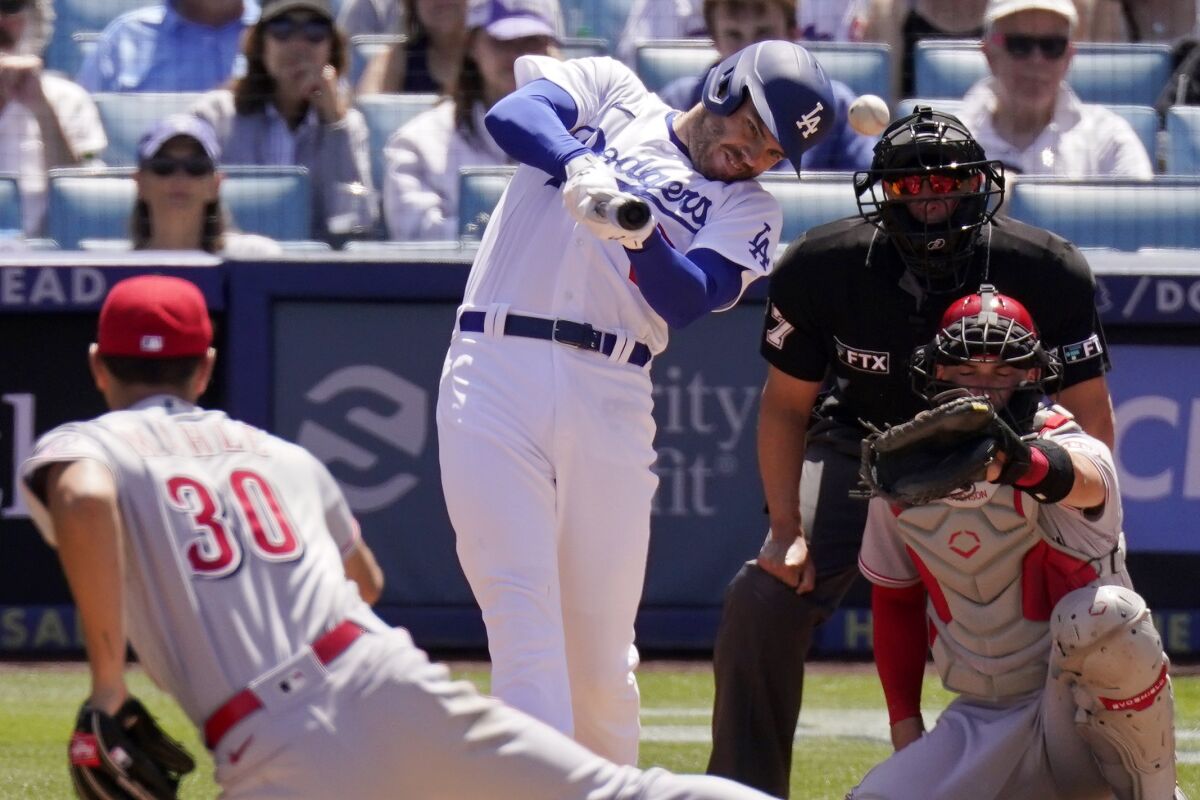 Los Angeles Dodgers' Freddie Freeman, second from left, hits a single as Cincinnati Reds starting pitcher Tyler Mahle, left, watches long with catcher Tyler Stephenson, right, and home plate umpire Jim Reynolds during the fourth inning of a baseball game Sunday, April 17, 2022, in Los Angeles. (AP Photo/Mark J. Terrill)