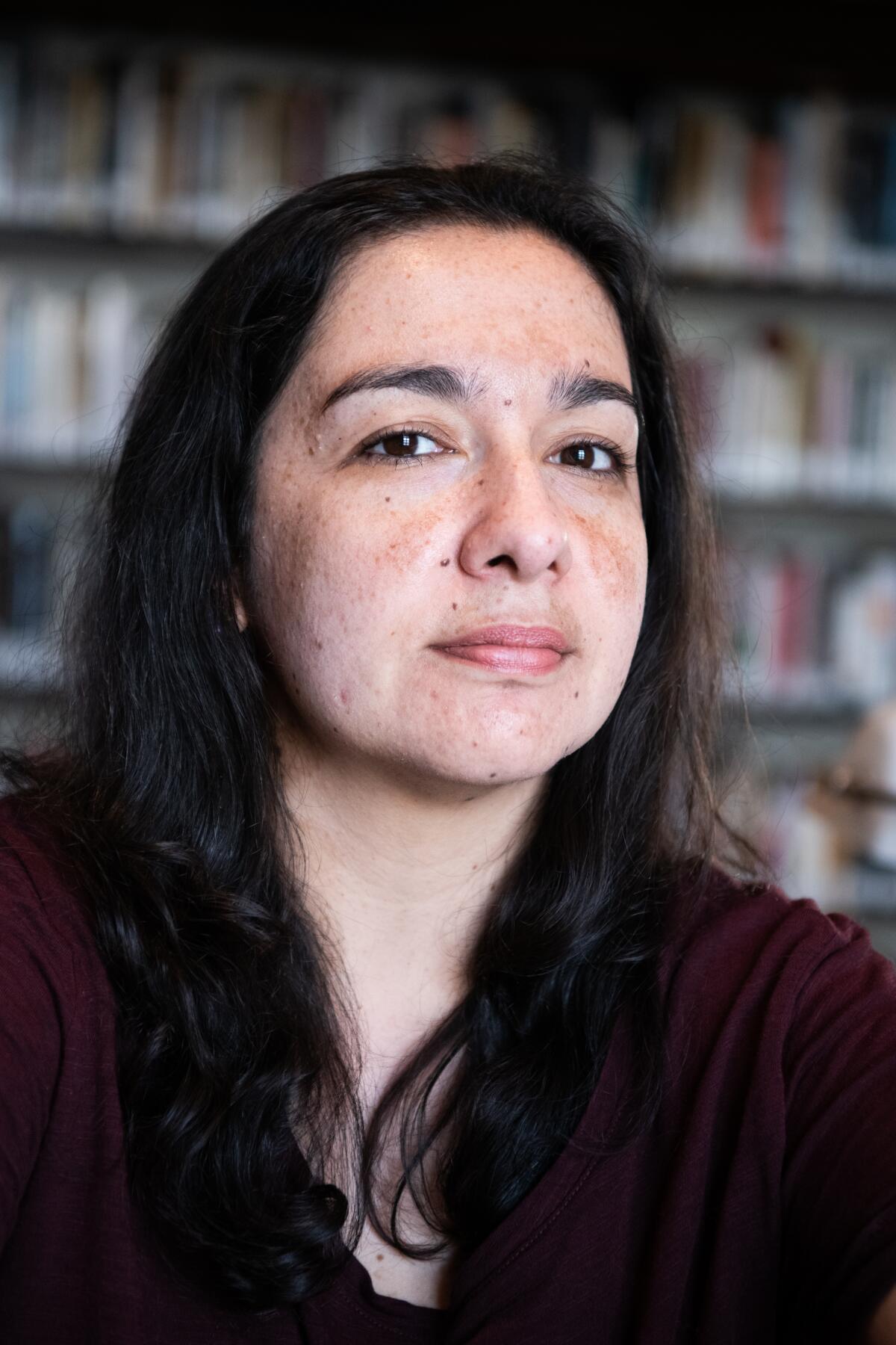 Mexican novelist Fernanda Melchor, seated in burgundy shirt in front of bookshelves.