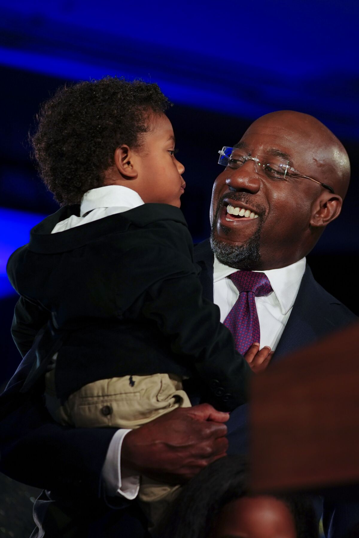 Sen. Raphael Warnock smiles and looks at his toddler son, whom he holds. 