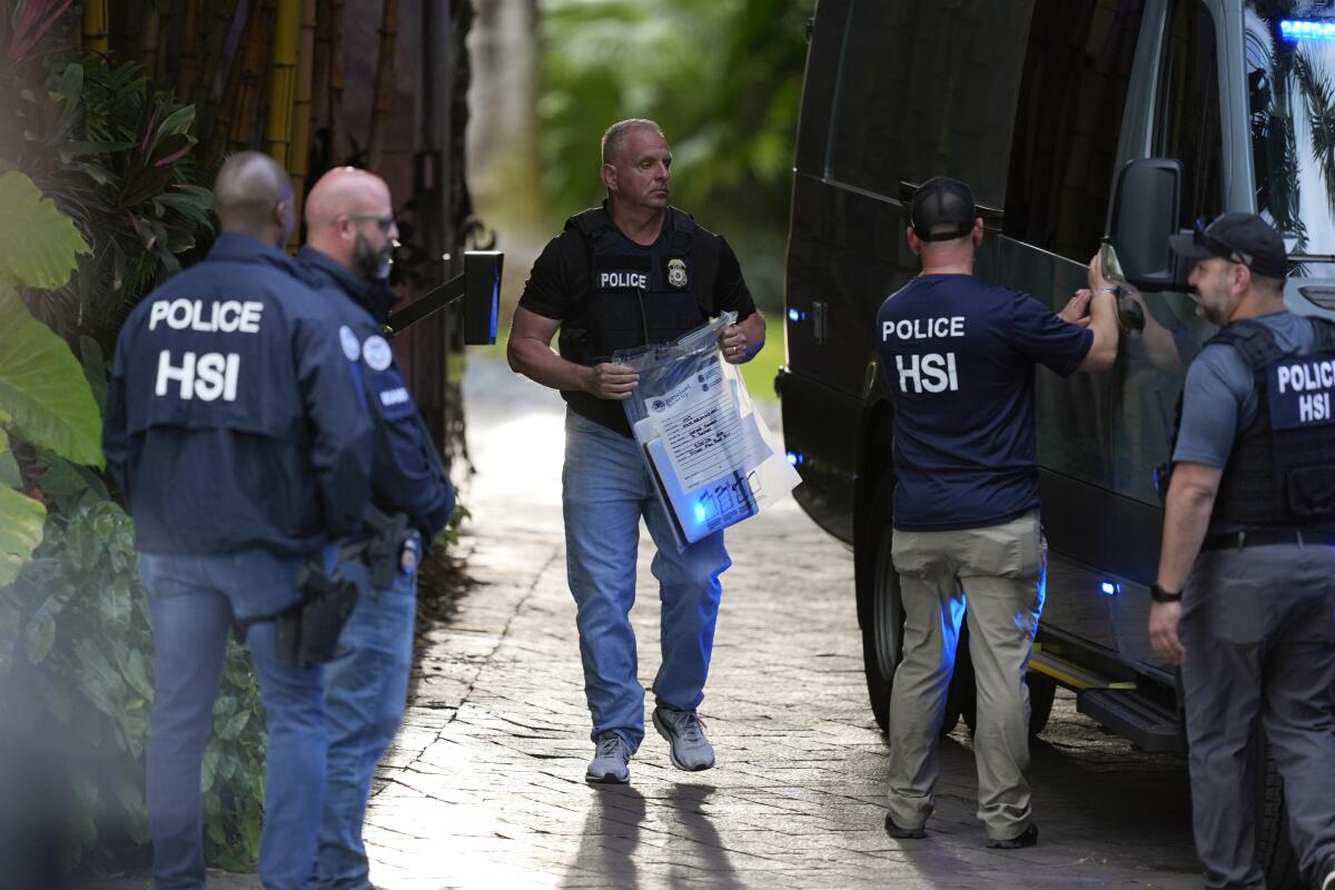A law enforcement agent carries a bag of evidence at the entrance to a property belonging to rapper Sean 