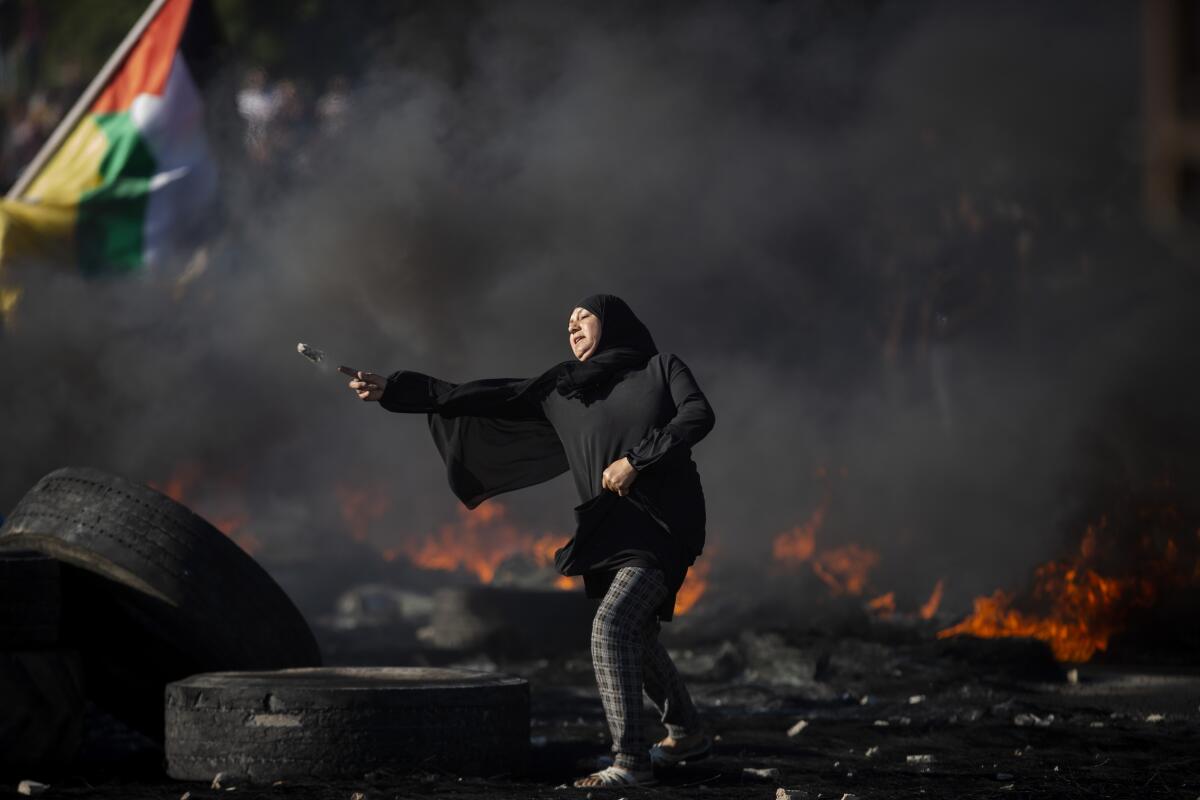 A woman stands amid burning tires. 