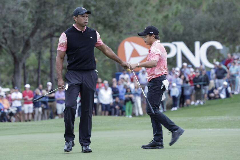 Tiger Woods extends his arm on the golf course and congratulates his son, Charlie, after finishing a round of golf