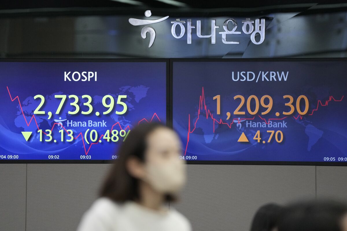 A currency trader walks near the screens showing the Korea Composite Stock Price Index (KOSPI), left, and the foreign exchange rate between U.S. dollar and South Korean won at a foreign exchange dealing room in Seoul, South Korea, Friday, March 4, 2022. Shares were lower Friday in Asia after another bumpy day on Wall Street, as investors remain concerned about the broader impact of Russia’s invasion of Ukraine. (AP Photo/Lee Jin-man)
