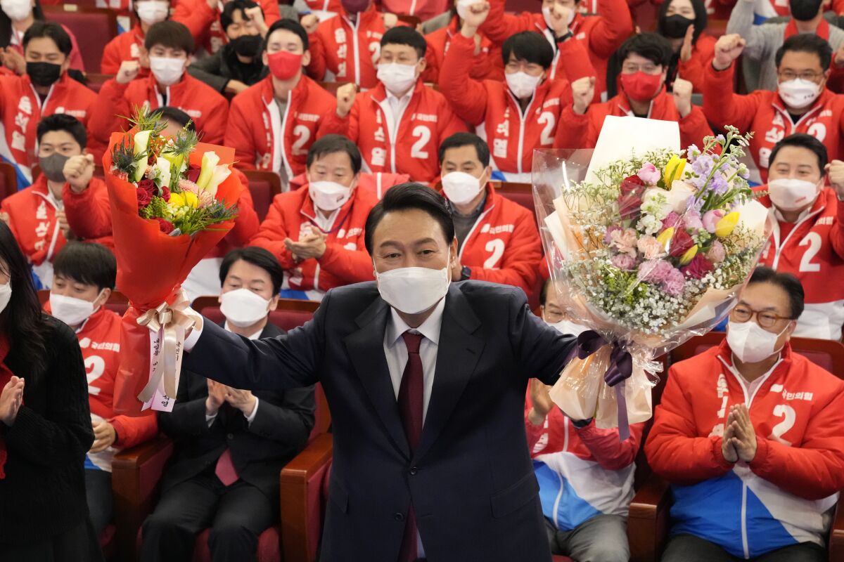 Yoon Suk Yeol, the presidential candidate of the main opposition People Power Party, who was elected South Korea's new president on Thursday, holds bouquets as he is congratulated by party's members and lawmakers at the National Assembly in Seoul, South Korea, Thursday, March 10, 2022. Yoon Suk Yeol, a conservative former top prosecutor, was elected South Korea's new president on Thursday, defeating his chief liberal rival in one of the country's most closely fought presidential elections. (AP Photo/Lee Jin-man, Pool)