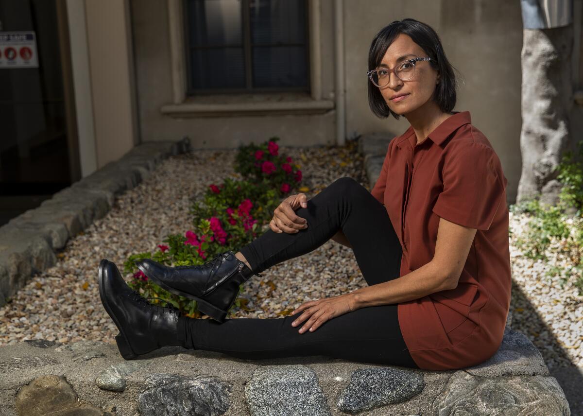 Carribean Fragoza sits on a stone wall outside a building on the grounds of Claremont Graduate University.