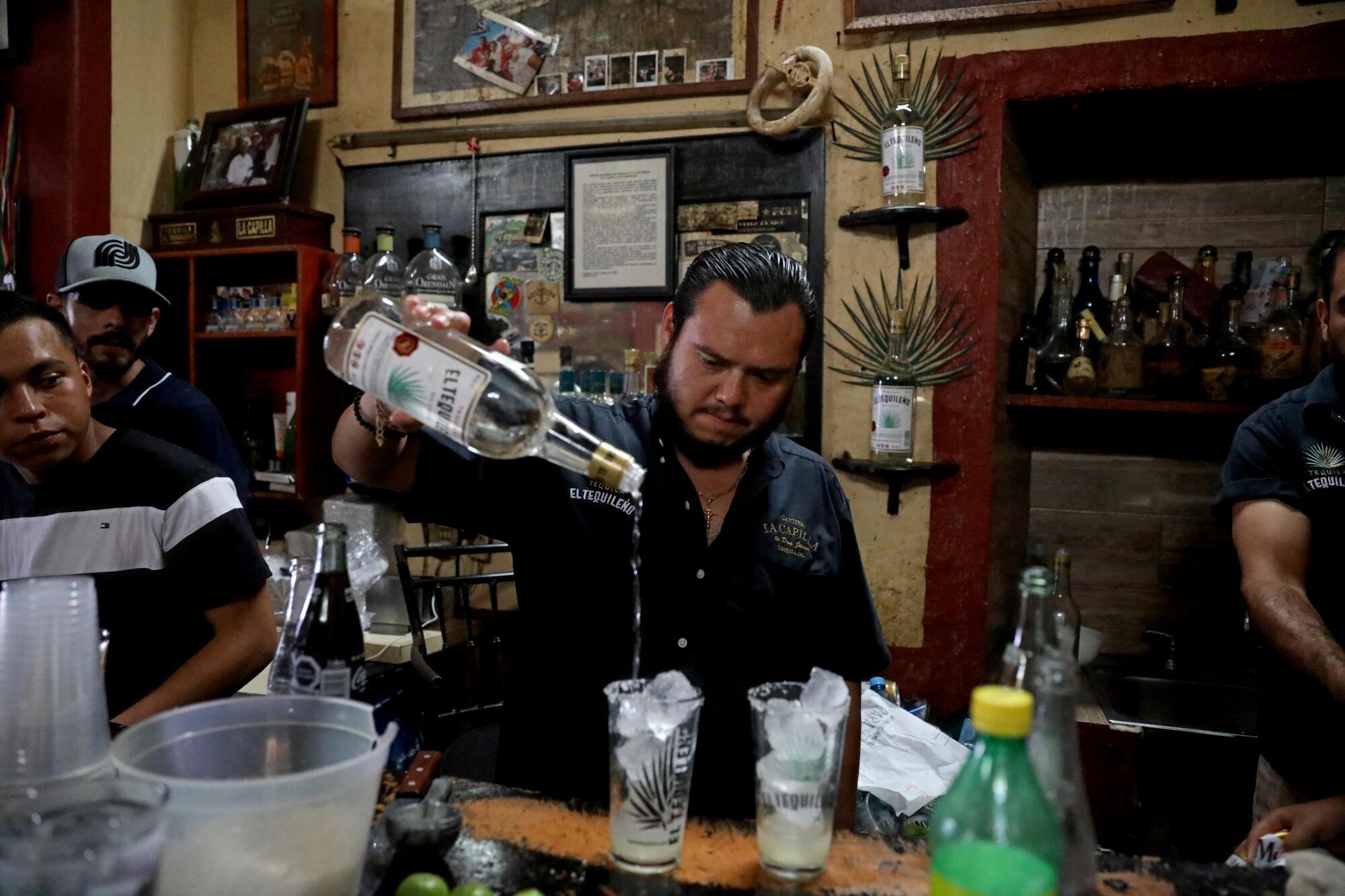 A bartender pours tequila into mixed drinks