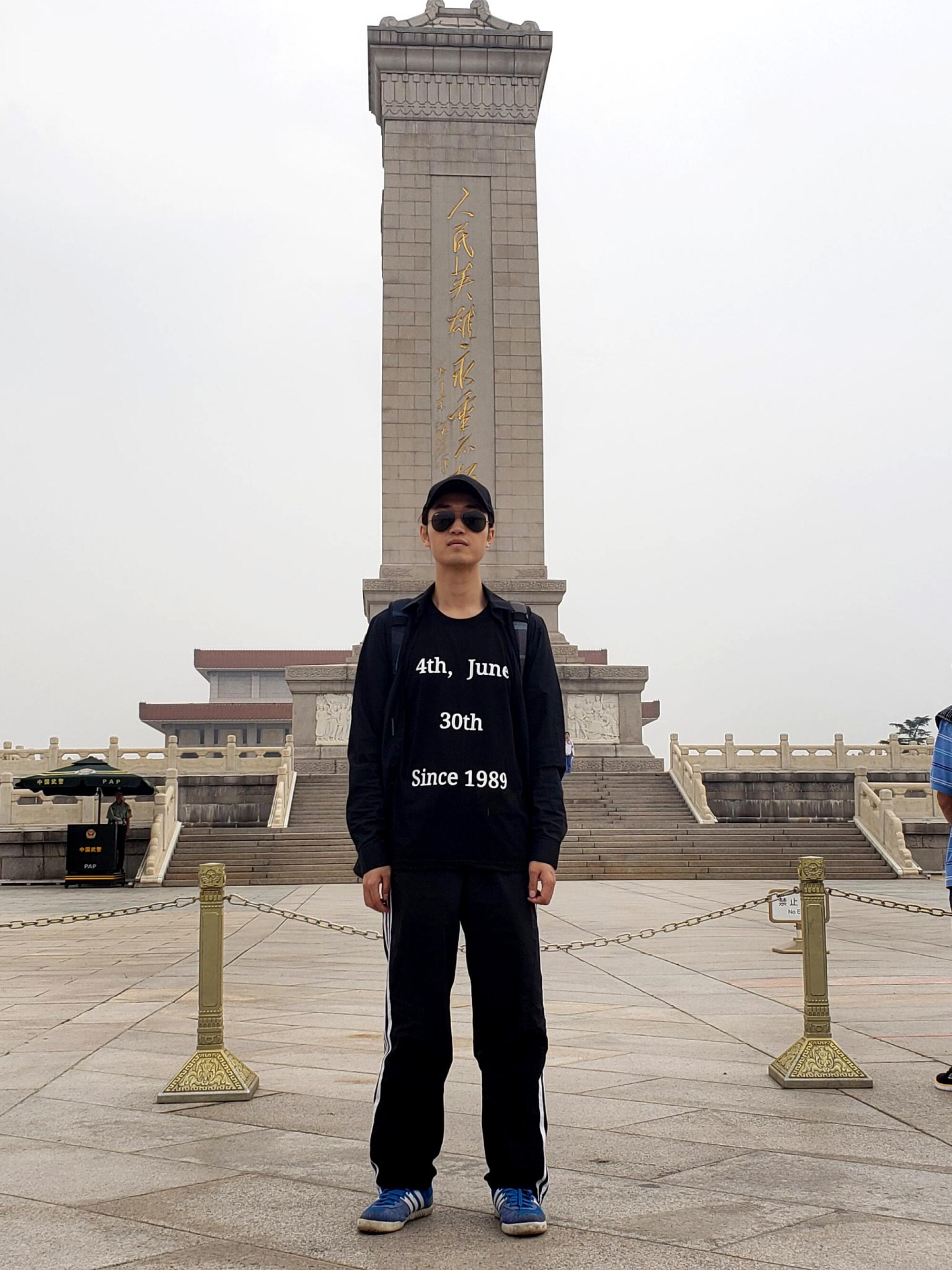 A man dressed all in black stands in front of a beige monument