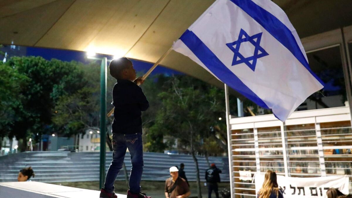 A boy waves the Israeli flag as African migrants and Israelis protest in Tel Aviv on April 9, 2018, against the government's attempt to forcibly deport African refugees and asylum seekers.