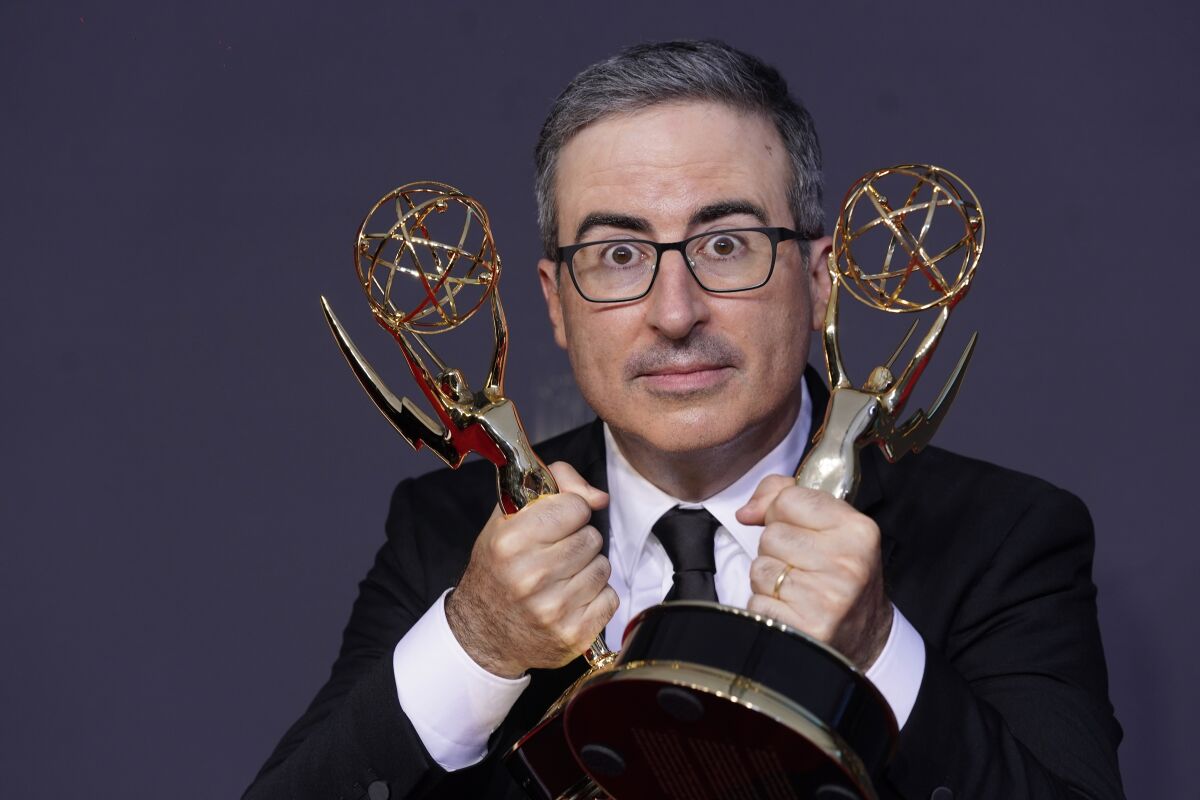 John Oliver holds an Emmy statuette in each hand.