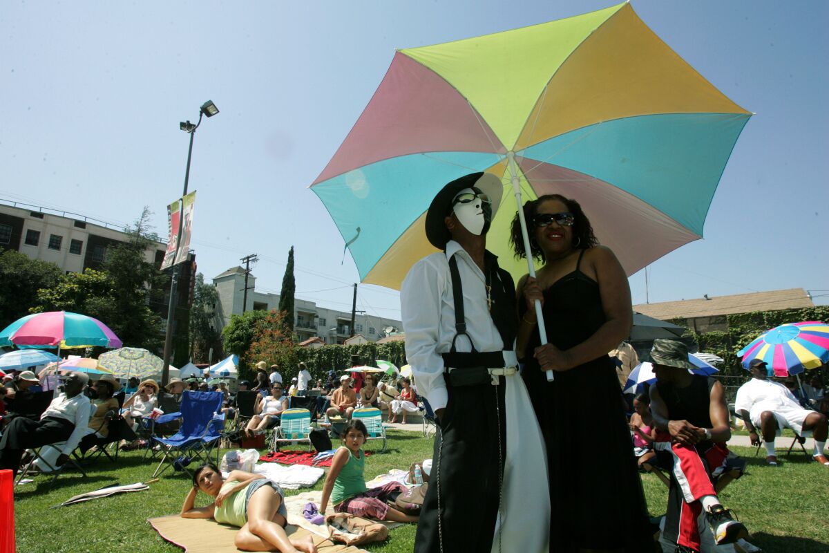 Two people in costume standing listen to music under an umbrella during the 12th Annual Central Avenue Jazz Festival