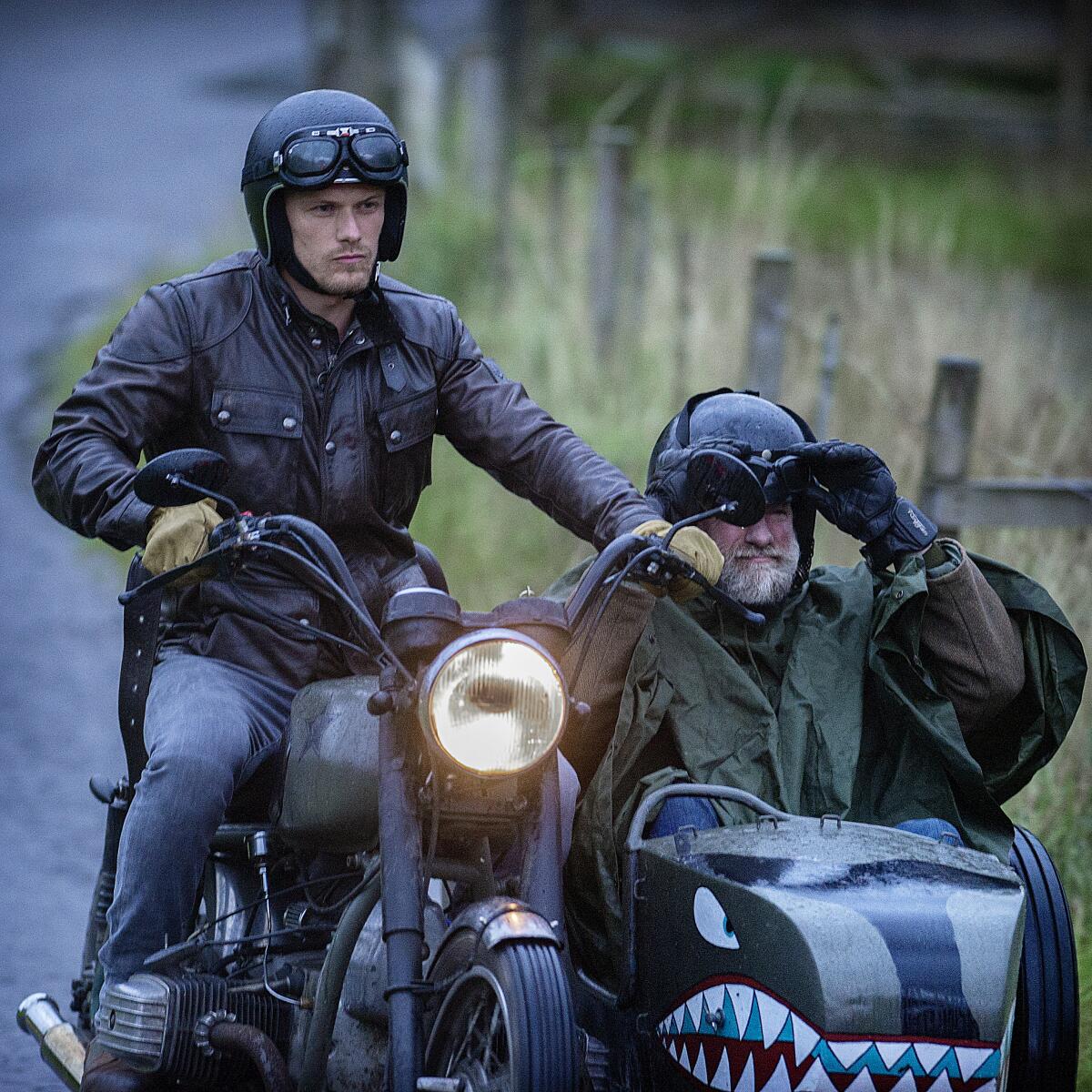 Sam Heughan on a motorbike and Graham McTavish in a sidecar.
