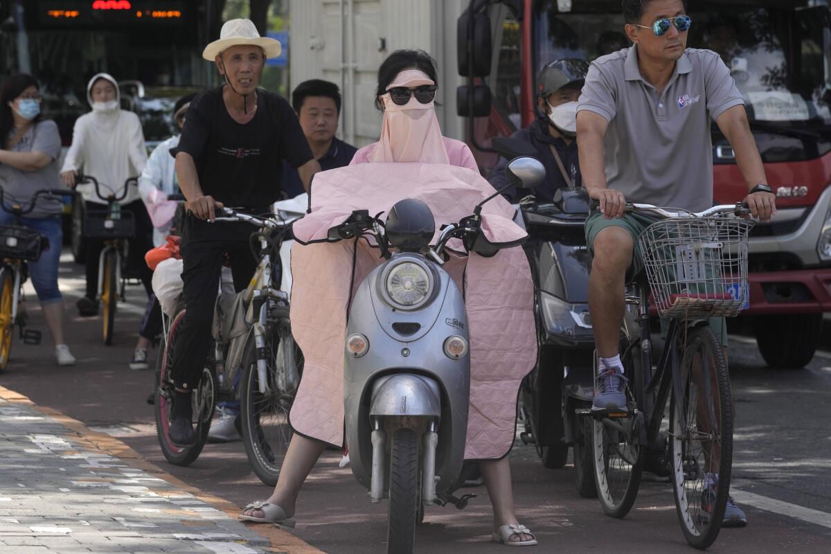 A woman covered up from the sun waits at a traffic junction, Wednesday, July 13, 2022, in Beijing. (AP Photo/Ng Han Guan)