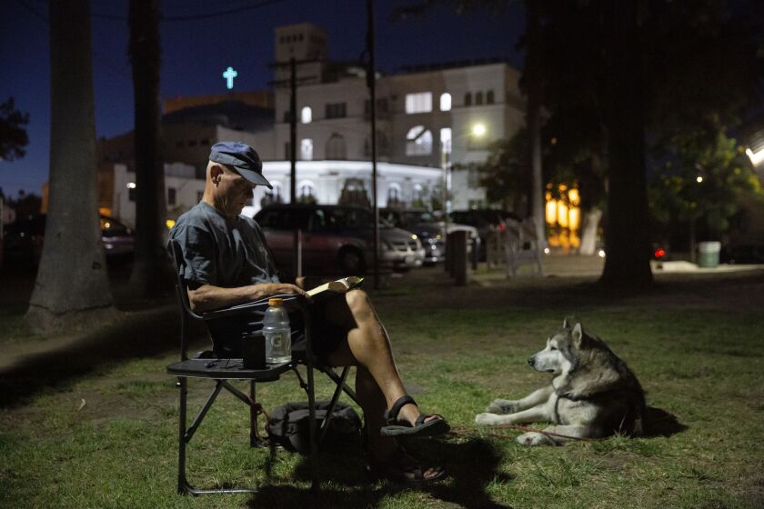 LOS ANGELES, CALIF. - AUGUST 01, 2019: Shane Isaacson, an army veteran who is experiencing homelessness, reads with his service dog, Bear, late into the night at Echo Park Lake in Los Angeles, Calif. on Thursday, Aug. 1, 2019. ÒHeÕs my best friend. I donÕt go anywhere without him,Ó Isaacson says of Bear. Two elected officials have called for statewide construction of shelters, and once they are built, homeless people such as Isaacson will have to vacate the streets. (Liz Moughon / Los Angeles Times)