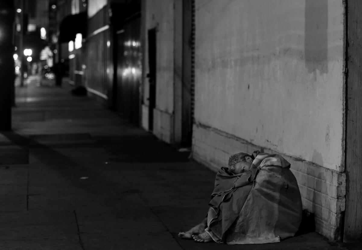 Wearing only a pair of boxer shorts, a beach blanket and nothing on his feet in the predawn hours, a man sits quietly on a sidewalk on skid row.