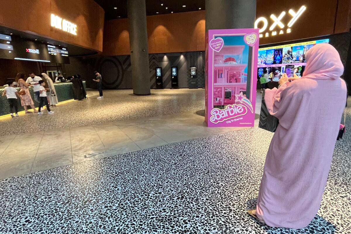 A woman in a pink robe stands at the entrance of a movie theater screening the film "Barbie"