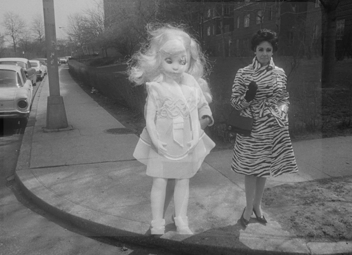A baby doll stands on a corner next to a real woman.