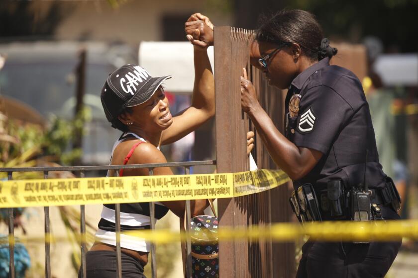 LAPD Sgt. Emada Tingirides, right, comforts the sister of a victim at the scene where two people were fatally shot in South Los Angeles.