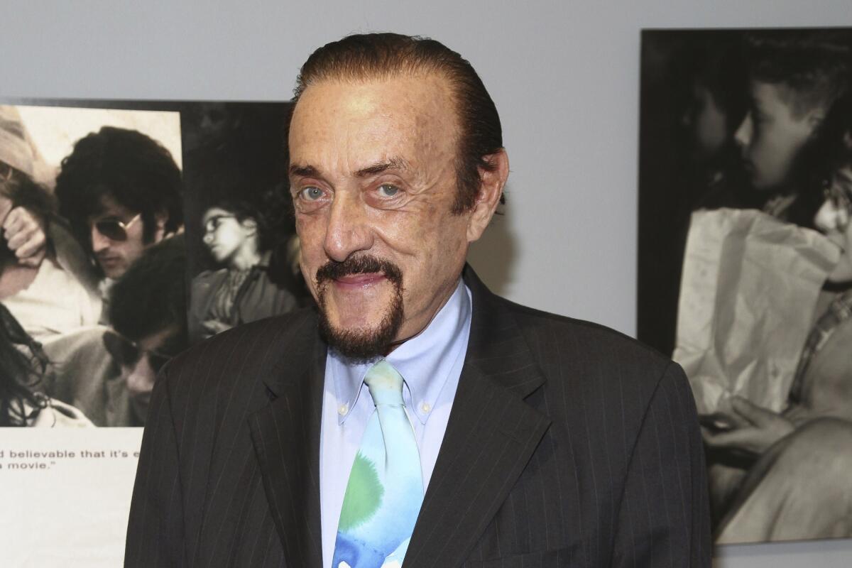 Philip Zimbardo, with goatee and wearing dark suit, lavender shirt and pastel tie, smiles for a photo.