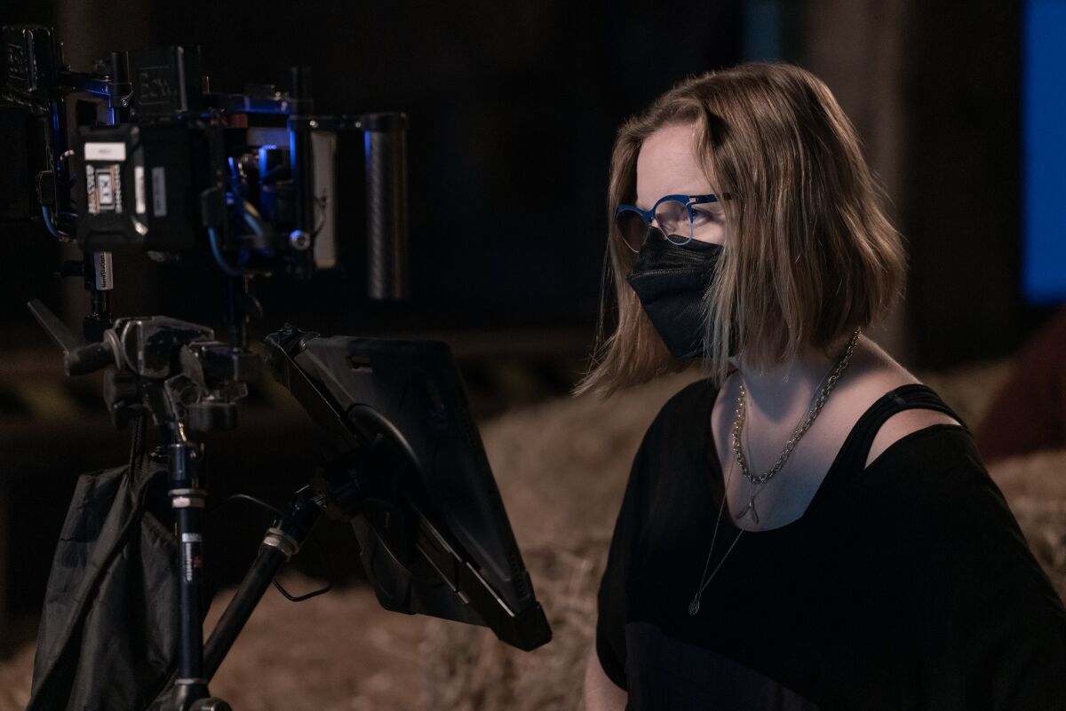 A woman wearing a COVID mask looks at the monitor of a movie camera.