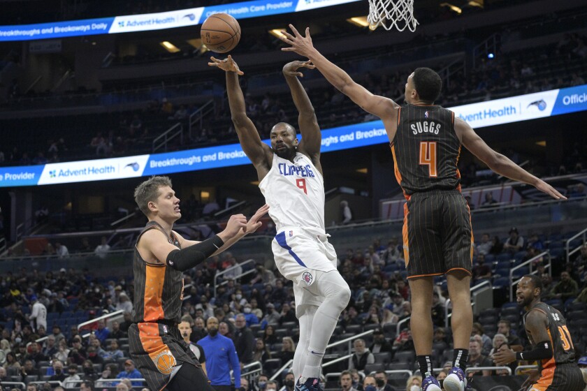 Clippers center Serge Ibaka passes the ball between Orlando Magic center Moritz Wagner and guard Jalen Suggs.