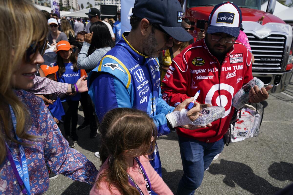 Chip Ganassi Racing driver Jimmie Johnson, center, of United States signs a an autograph for a fan before an IndyCar auto race at the Grand Prix of Long Beach on Sunday, April 10, 2022, in Long Beach, Calif. Johnson's right hand was injured in a crash on Friday. (AP Photo/Ashley Landis)