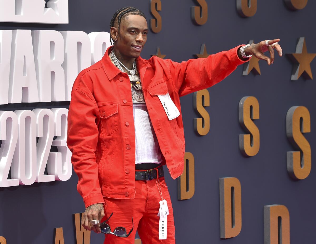 Soulja Boy in a red jacket and pants holding out his left arm and pointing in front of him