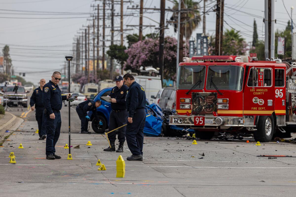 Authorities stand next to evidence markers in the street next to a wrecked car and a firetruck