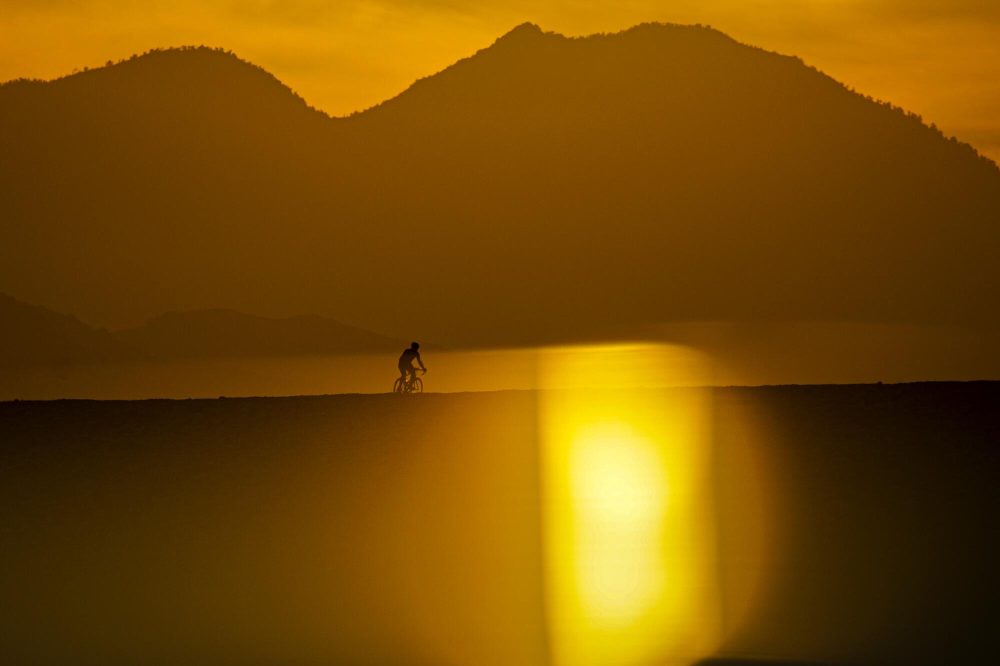 Sunrise over hills and a lone cyclist in silhouette